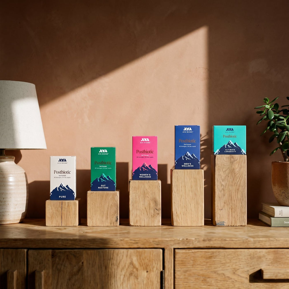 The five AYA BIOME™ boxes, PURE, Gut Restore, Women's Wellness, Men's Wellness and Ultimate Longevity, standing on oak blocks of rising height on a wooden sideboard