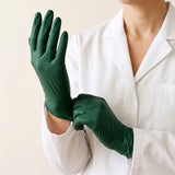 A person in a white coat pulling on dark green gloves