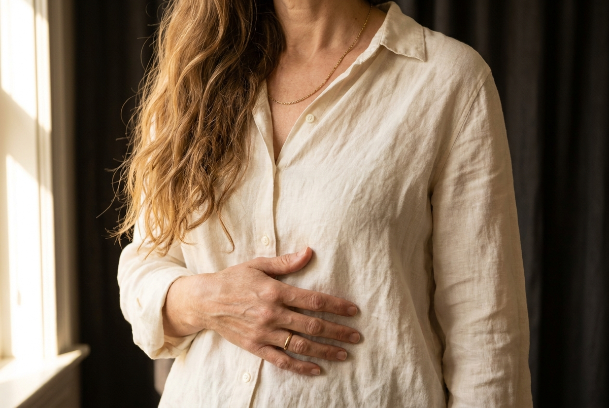 Woman with long hair in a cream linen shirt, one hand resting on her stomach