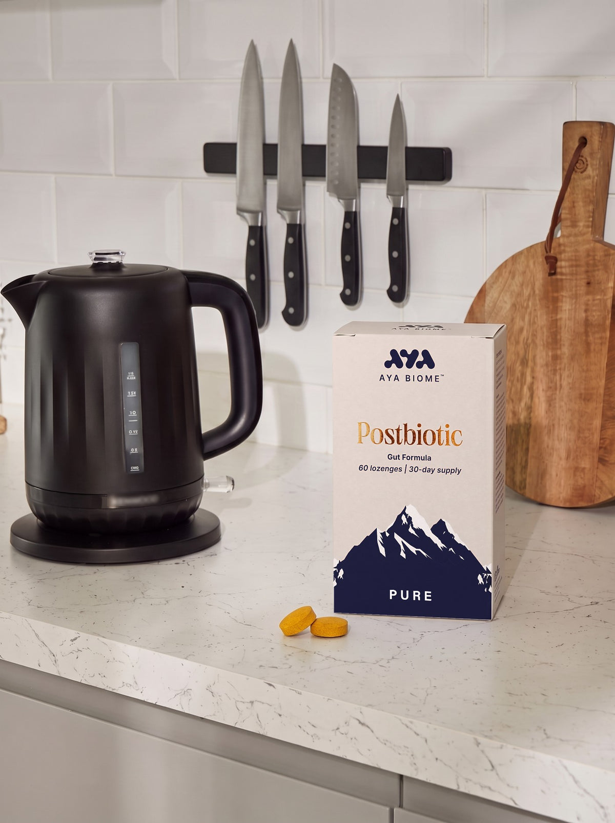 An AYA BIOME™ PURE box and two chewable tablets beside a black kettle on a marble kitchen worktop