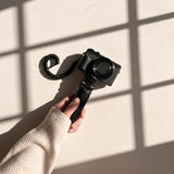 A hand in a cream sleeve holding up a compact camera against a sunlit wall