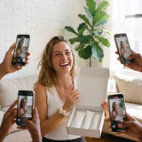 A laughing woman with an open box, filmed on phones by people around her