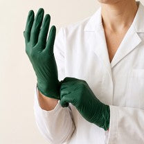 A person in a white coat pulling on dark green gloves